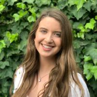 A person smiling in front of a leafy green background.