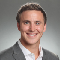 A man in a grey suit smiling against a plain background.