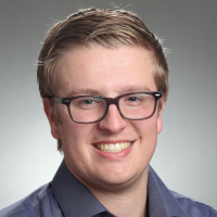 A person wearing glasses and a blue shirt, smiling at the camera.