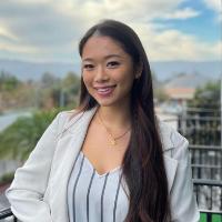A woman smiling outdoors with cloudy sky background.