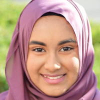 Person wearing a purple hijab smiling outdoors.