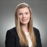 A person in business attire with a neutral background.