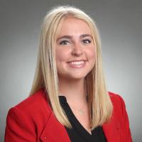 A woman in a red blazer smiling with a grey background.