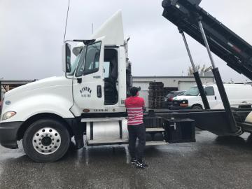 A person stands near a white hauling truck in a wet parking lot.