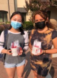Two people outdoors wearing masks, holding cups with straws.