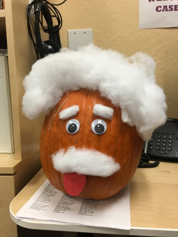 Decorated pumpkin with googly eyes, white fluffy eyebrows, mustache, and hair, sticking out tongue.