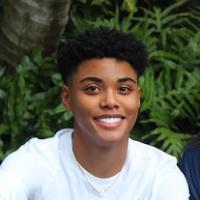 A smiling person wearing a white shirt in front of green leaves.
