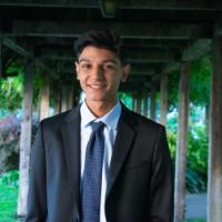 A person in a suit standing under a wooden pergola.