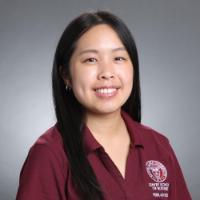 A person smiling, wearing a maroon shirt with a logo.