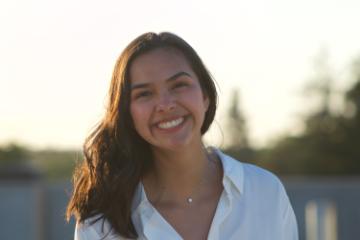 A person smiling outdoors during sunset.