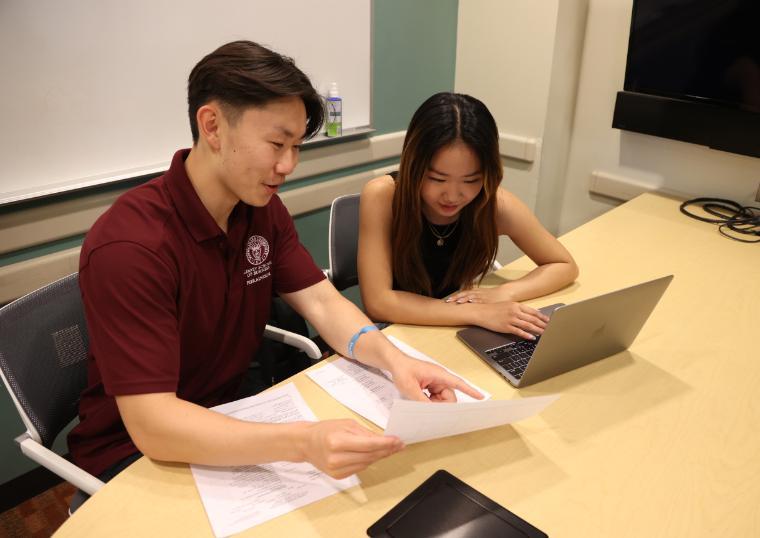 Two people reviewing documents and a laptop at a table.