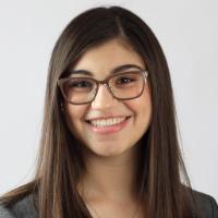 A woman wearing glasses, a yellow top, and a grey blazer.