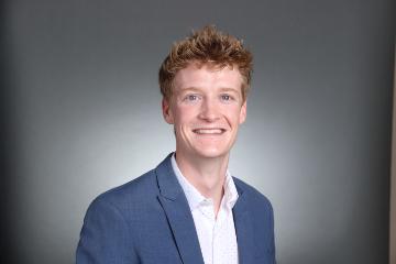 A person in a blue jacket and white shirt smiles in a portrait.