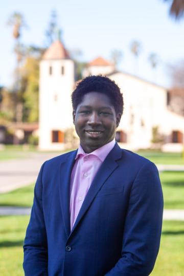Man in a suit smiling outdoors near a building.