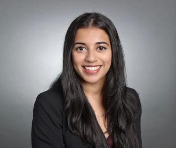 A person smiling in a professional setting against a grey background.