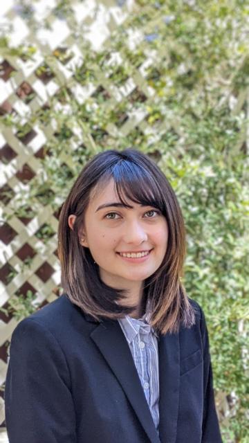 A person smiling in front of a lattice with greenery.