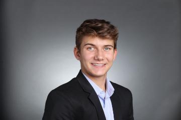 A person wearing a suit against a grey background.