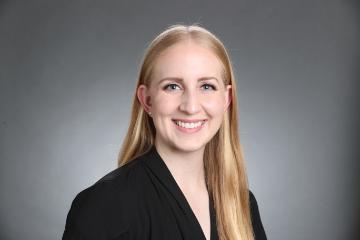 A person smiling in a professional headshot against a gray background.