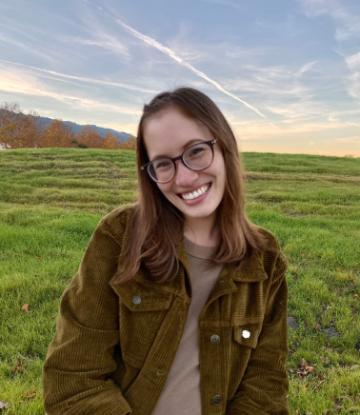A person in glasses smiling in an open grassy field.