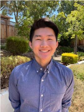 A person in a blue shirt standing outside with greenery in the background.