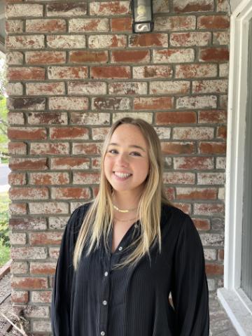 A person smiling in front of a brick wall.