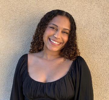 A person smiling while wearing a black top standing against a beige wall.