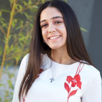 A woman smiling in a white top with a pink flower print.