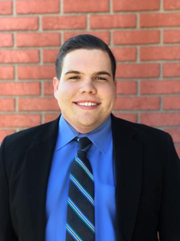 Smiling man in business attire standing against a brick wall.