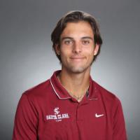 A person in a maroon collared shirt with sponsorship logos.