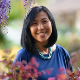 A person smiling surrounded by purple flowers.