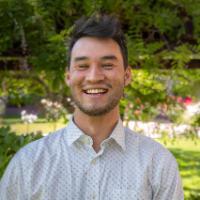 Man wearing a striped shirt smiling in a garden.
