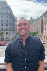 A person in a blue shirt smiling in an urban setting.