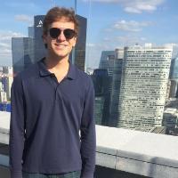 Person in blue shirt wearing sunglasses with cityscape background.