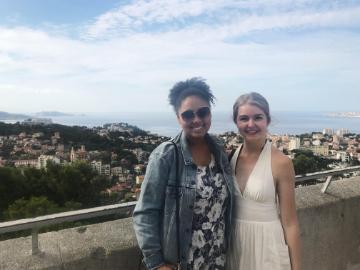 Two individuals posing with a scenic cityscape background.