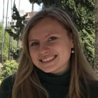 Person smiling outdoors with trees in the background.