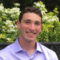 A person in a light purple shirt sits outdoors.