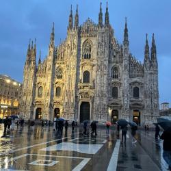 Gothic-style cathedral with illuminated facade reflected on wet pavement under an evening sky.