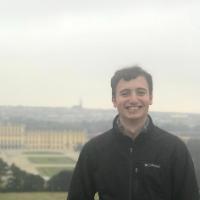 A person smiling with a large building complex in the background.