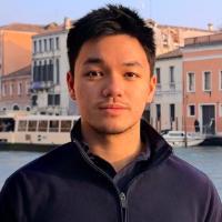 A person stands in front of water and buildings.