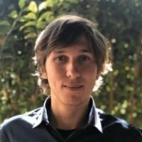 A person outdoors with greenery in the background.