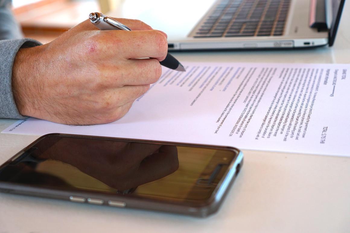 A man reviewing a contract; near laptop and smartphone