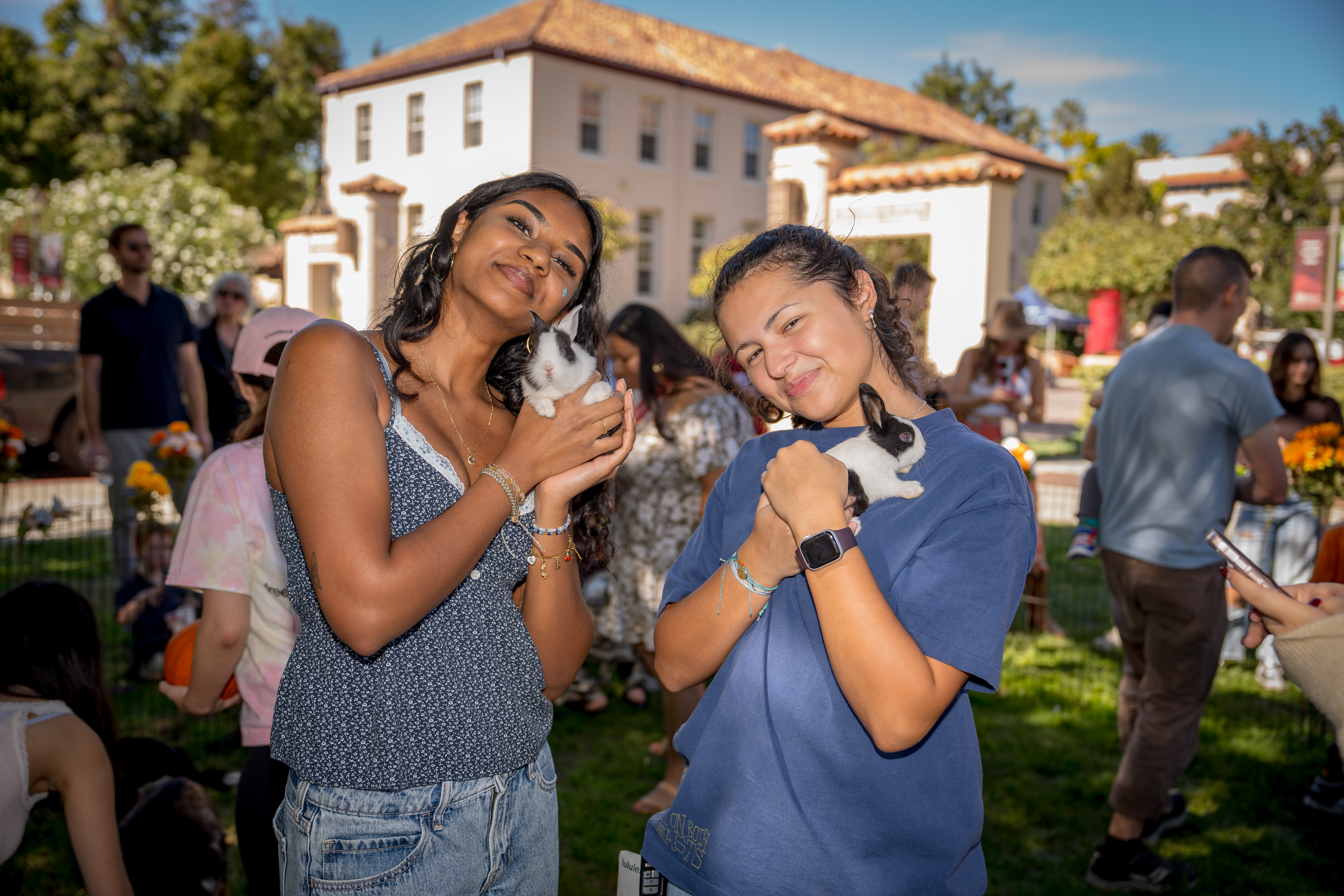Two women smile at the camera while holding up rabbits