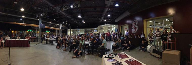 A large crowd seated indoors, watching a stage performance.