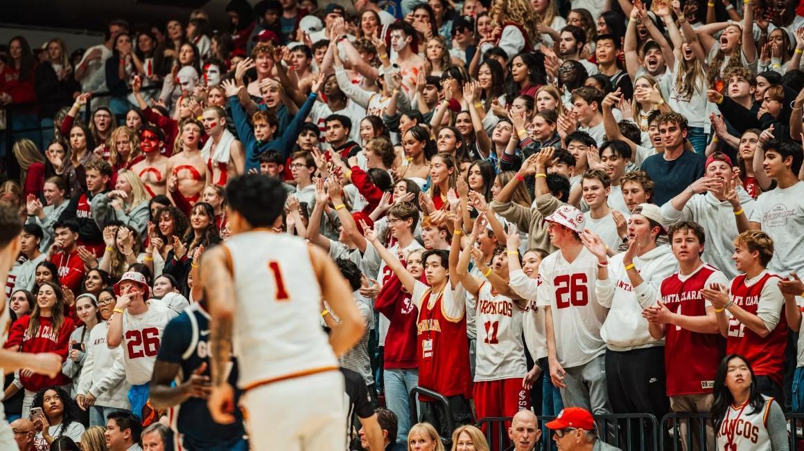 a Broncos player jogs by a large crowd of cheering students at a basketball game
