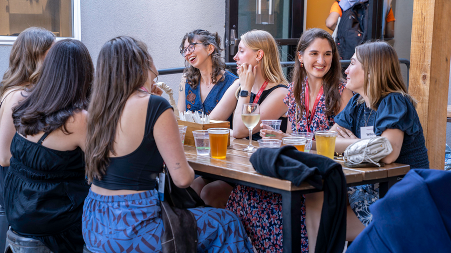 A large group of young women sitting around a table enjoying beers and talking 