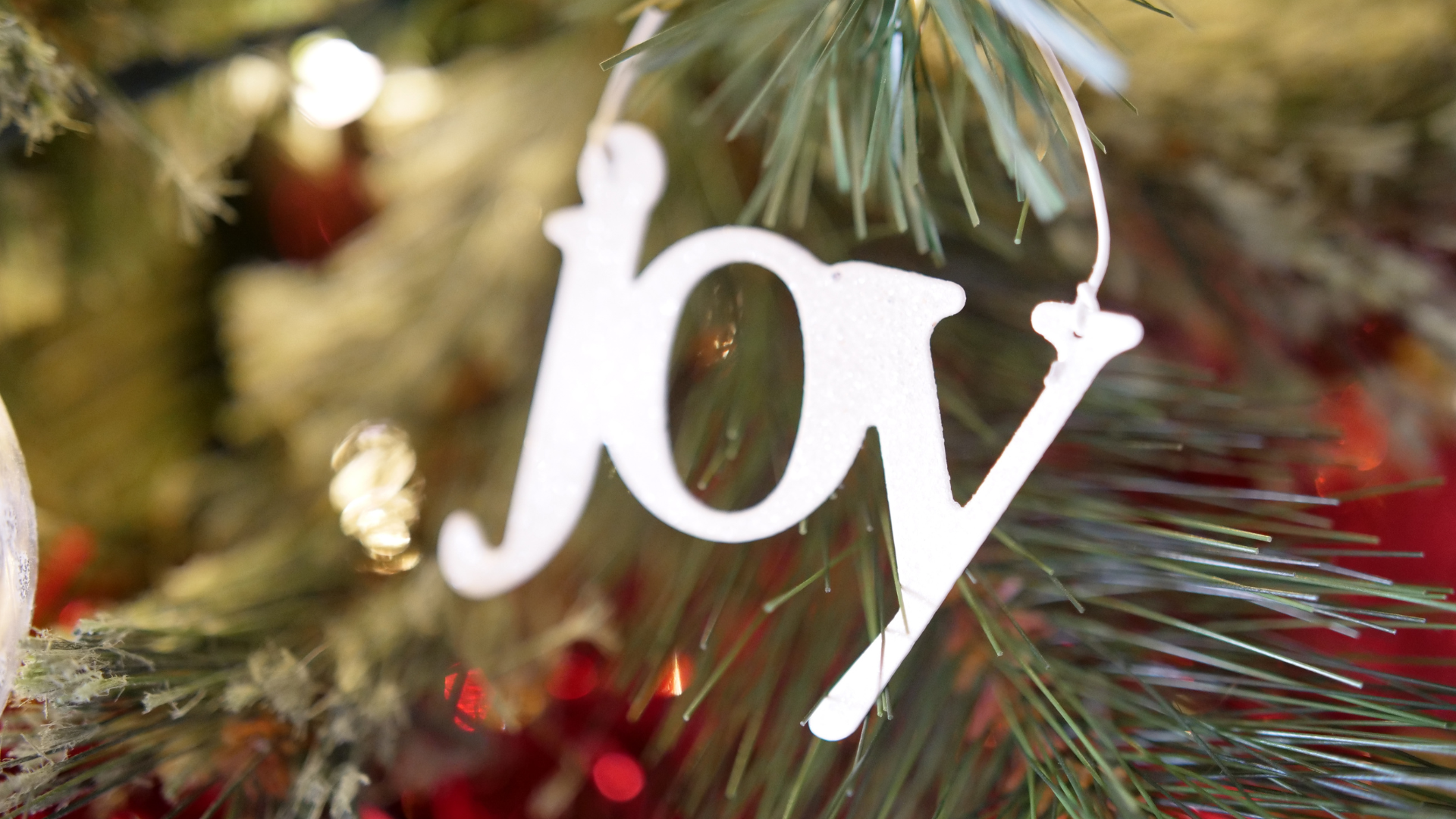 Joy Christmas ornament hanging from a tree