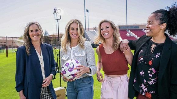 Four women standing on a soccer field.
