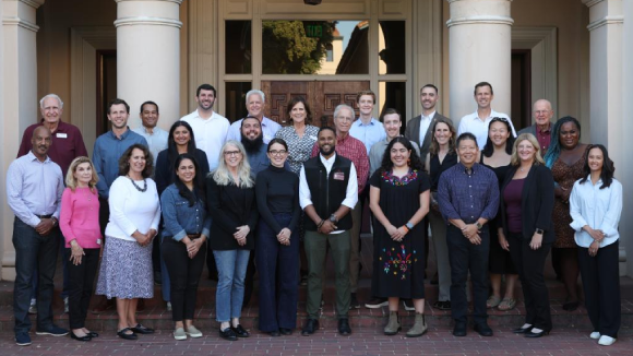A group of smiling people posing outside Nobili Hall on the Santa Clara campus.