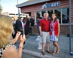Woman taking a photo of a dad and grad in front of The Hut.
