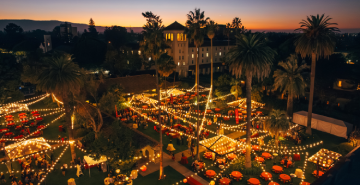 An overhead view of the Grand Reunion class parties in SCUs Mission Gardens. String lights bathe tables and attendees in a golden light, and the sun sets behind Nobili Hall. 